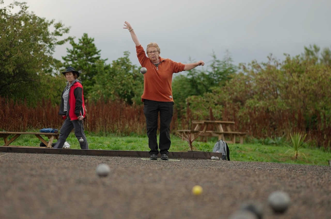 Petanque player stood and mid throw, with ball heading towards camera