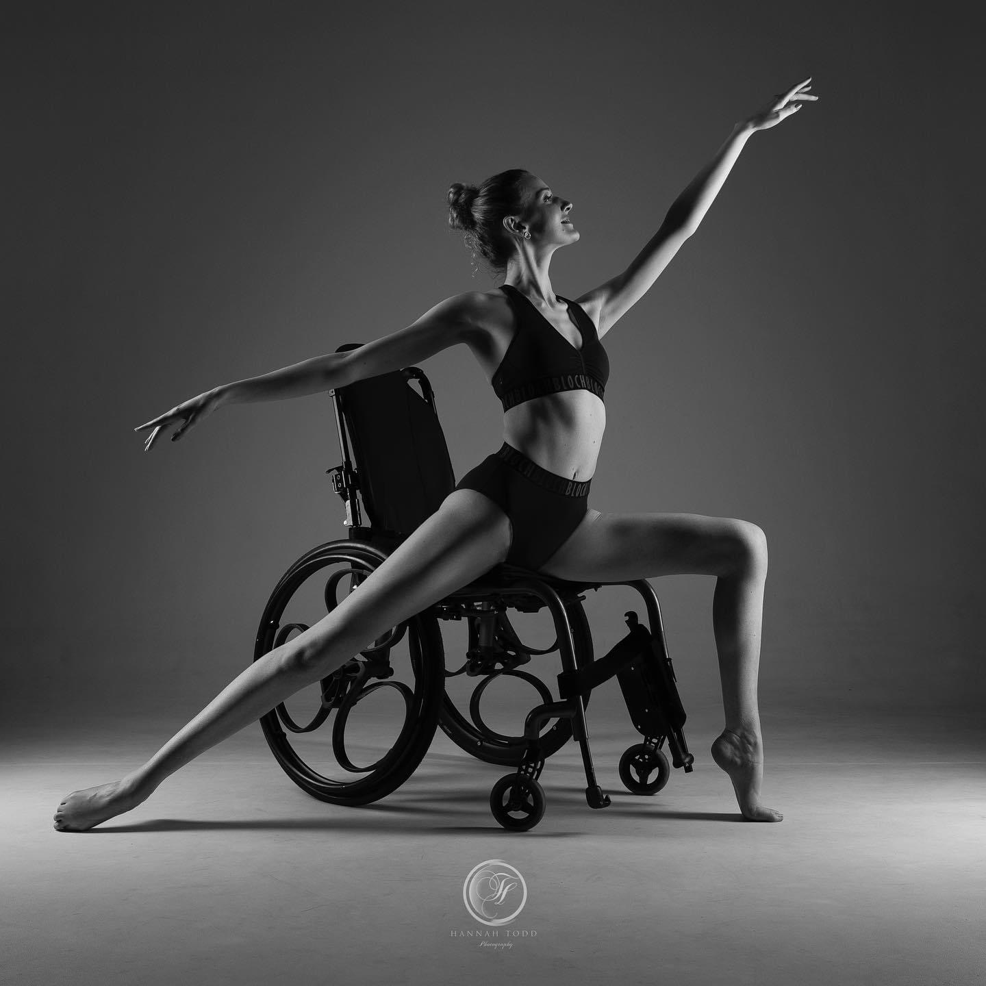 A ballerina in a wheelchair in an arabesque pose. The photo is in black and white.