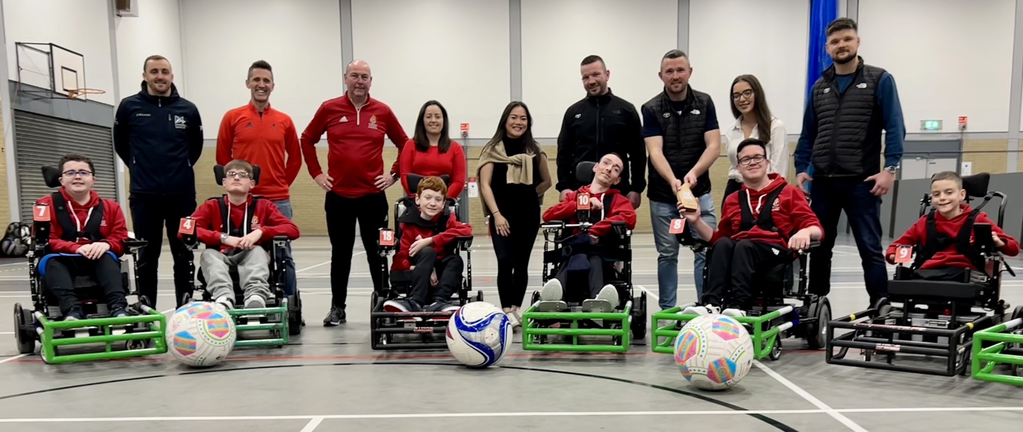 Award hand over with Trailblazers powerchair football club. Full squad are sat in their powerchairs in the first row, with club staff and representatives from ParalympicsGB, DSNI, Every Body Moves and Toyota stood behind. Photo taken in an indoor sports hall.