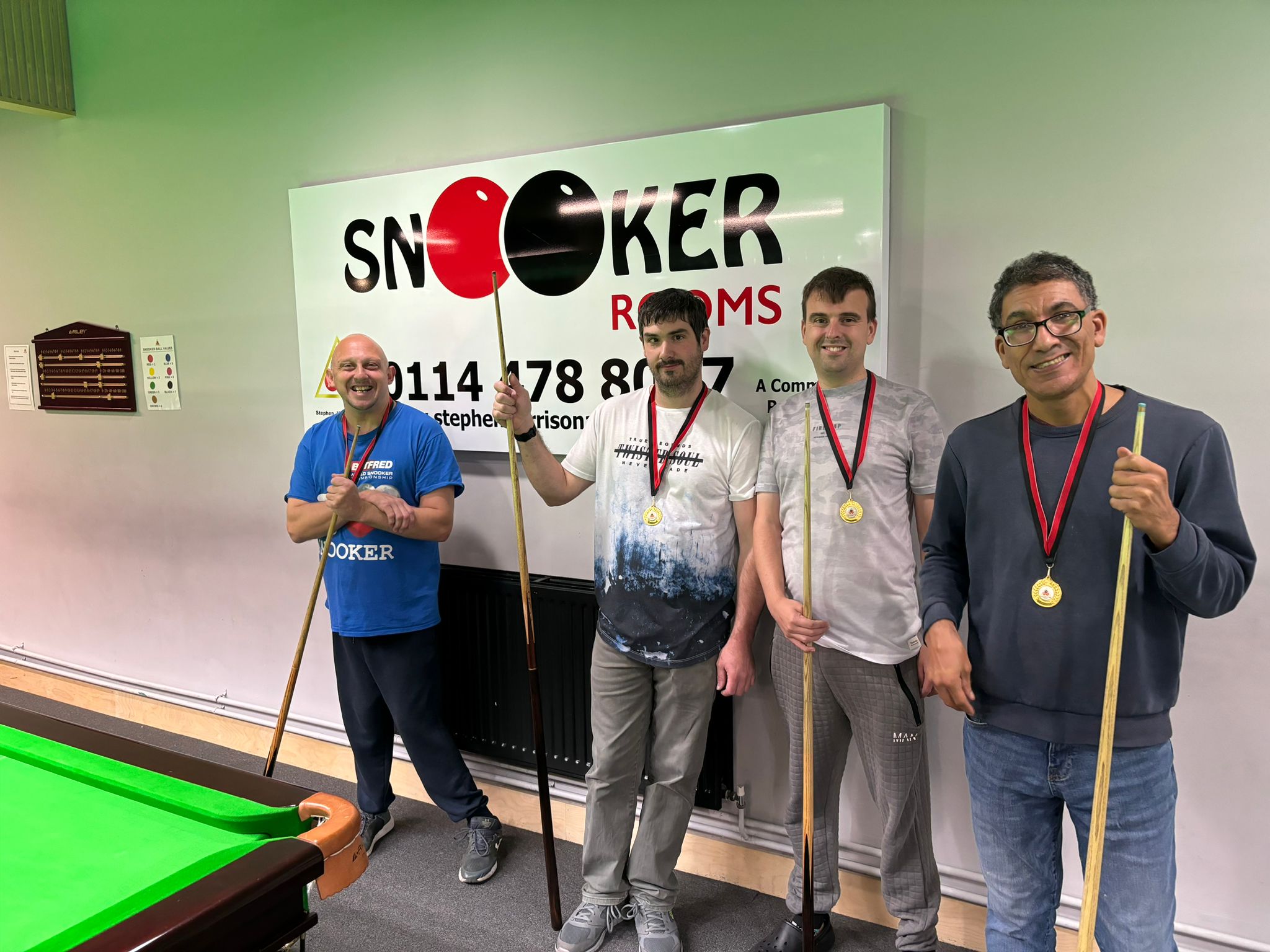 Four members of the Stephen Harrison Snooker Academy pose for a photo with cues in front of a snooker table