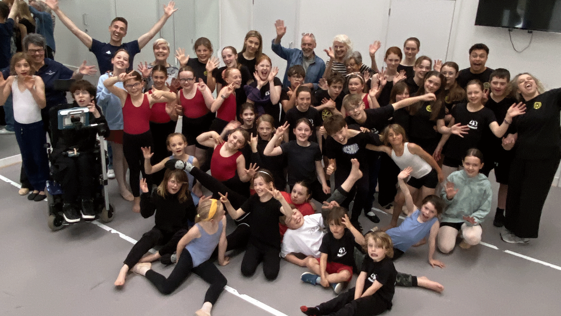 Full group shot of Cairngorm School of Dance participants in a mixture of stood and sat poses, all smiling and waving towards the camera.