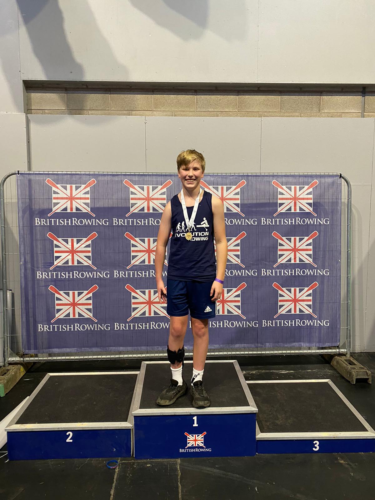 Isaac stands on the podium with a gold medal around his neck at a British Rowing event