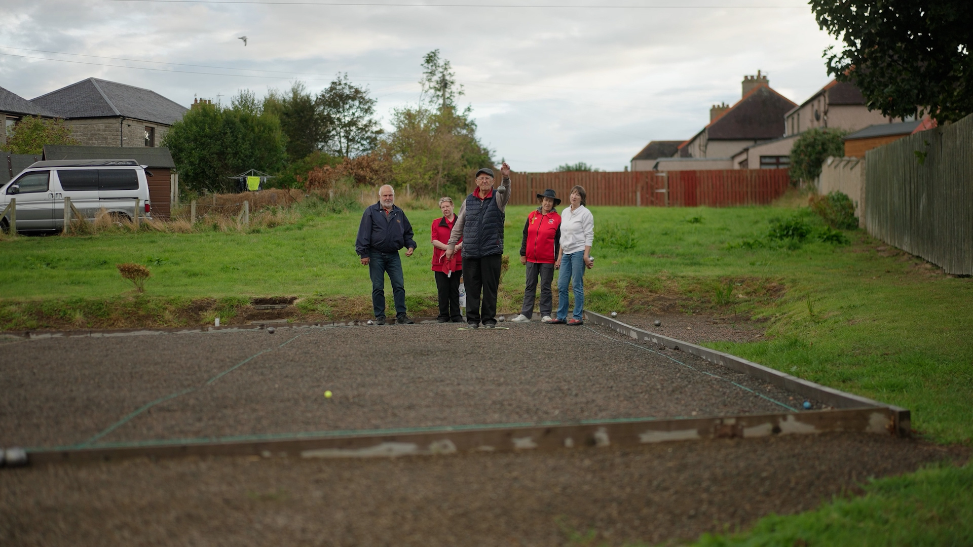 A game of petanque, with group of people stood at the end of the play area and throwing balls back towards the camera.