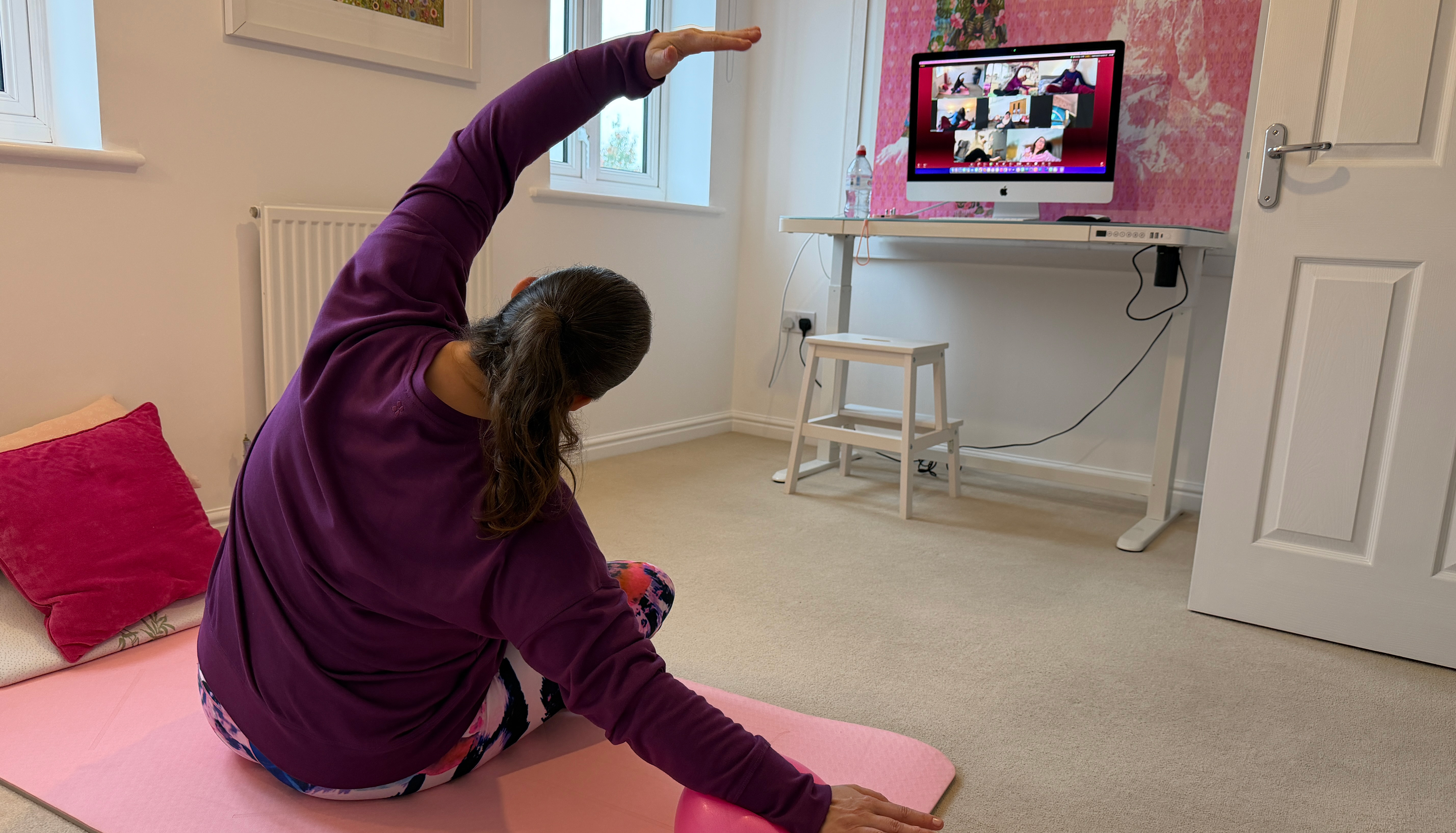 Instructor delivering an online adaptive pilates session - sat on the floor facing away from the camera with computer screen in front of them