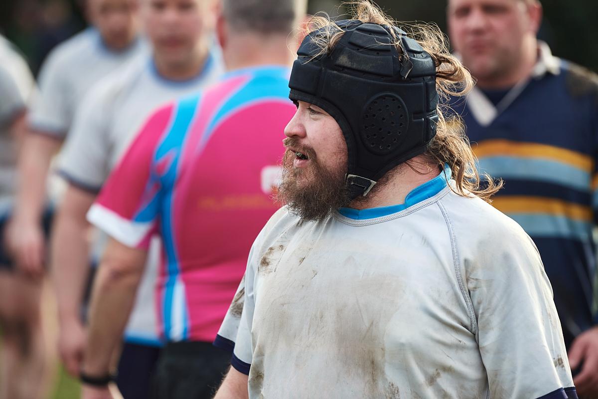 A male rugby player with a beard wearing a scrum hat in the midst of a game.