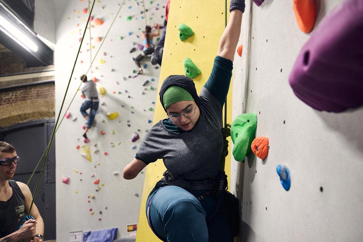 An adaptive climber mid climb on an indoor wall.