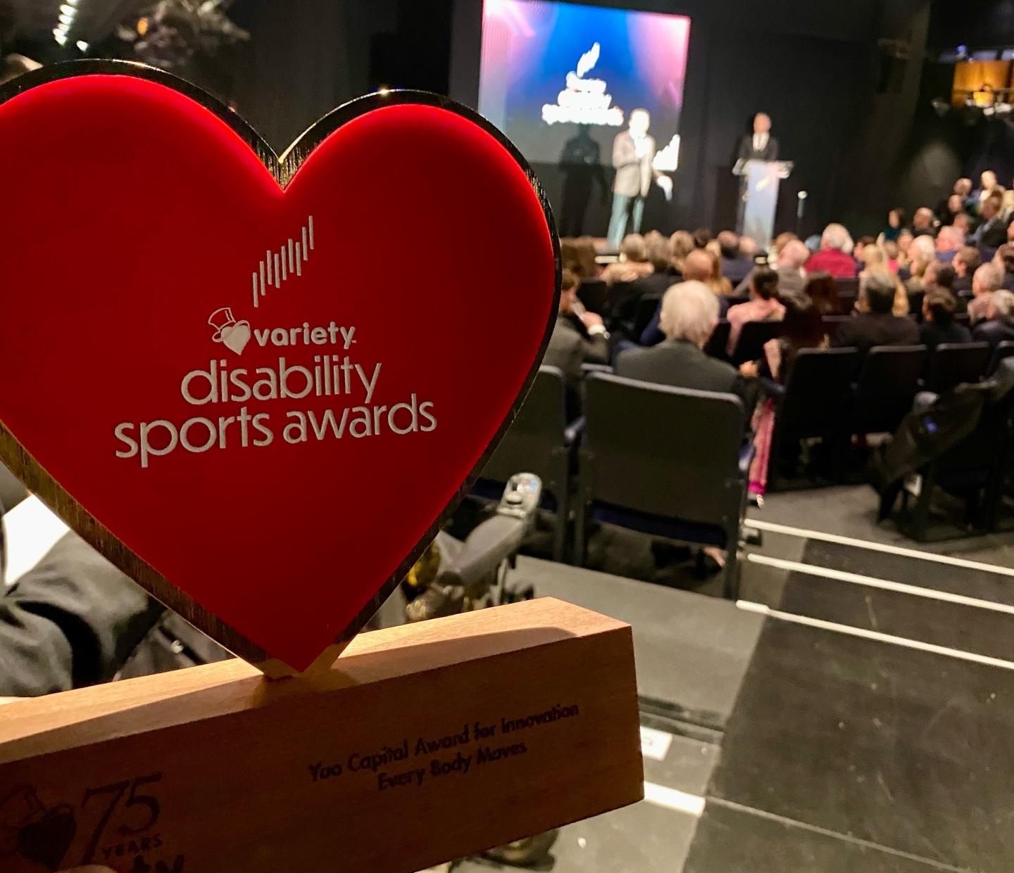 Image of the heart shaped variety disability sport award trophy in the foreground, with the stage blurred in the background.