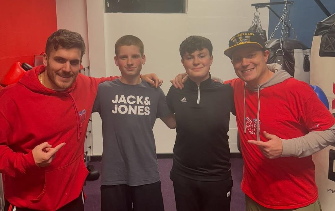 Dan Powell with three young boxers, all looking at the camera with their arms around each other