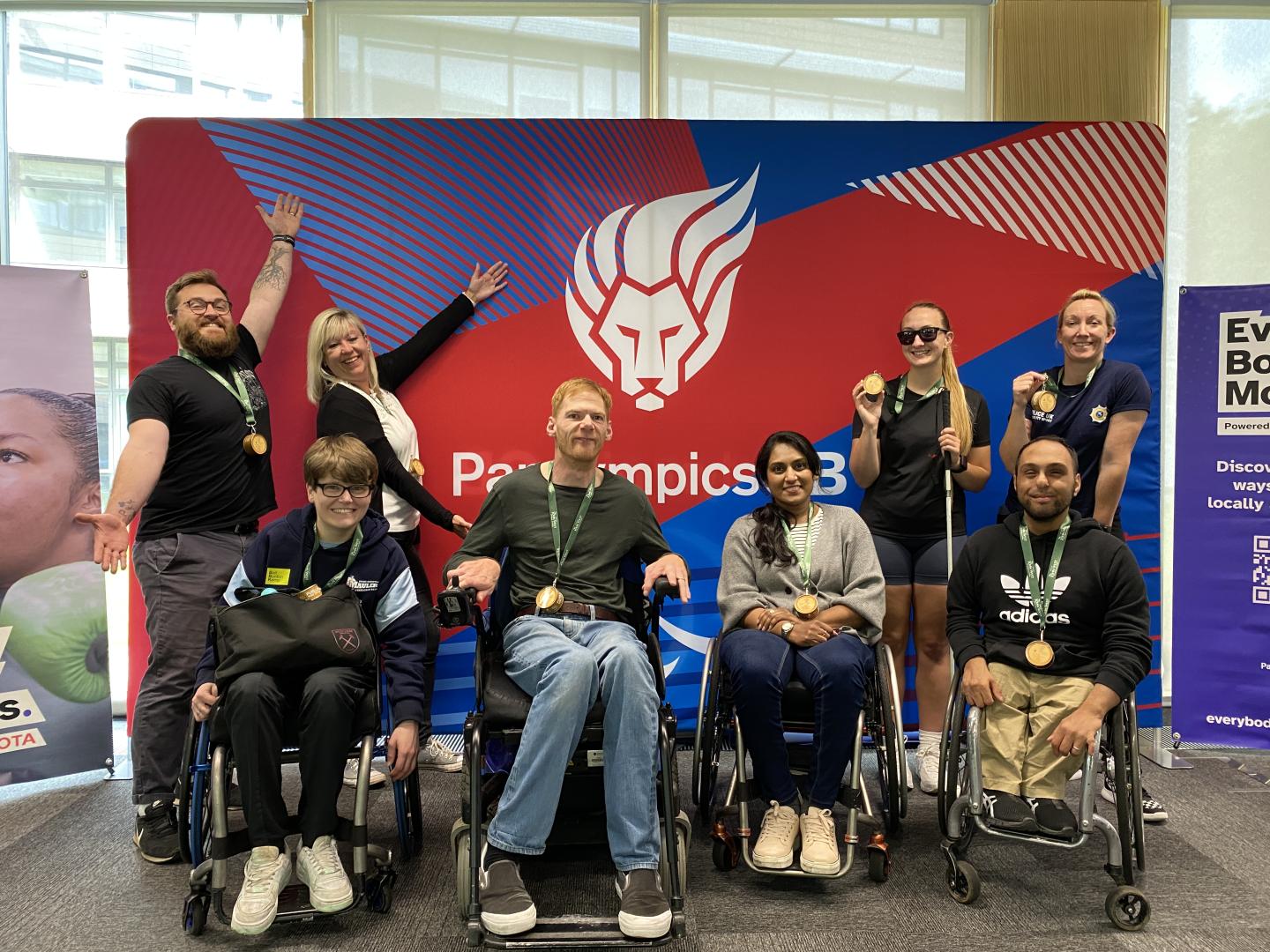 The LAB at kitting out are pictured smiling with their arms up infront of a Paris ParalympicsGB branded backdrop.