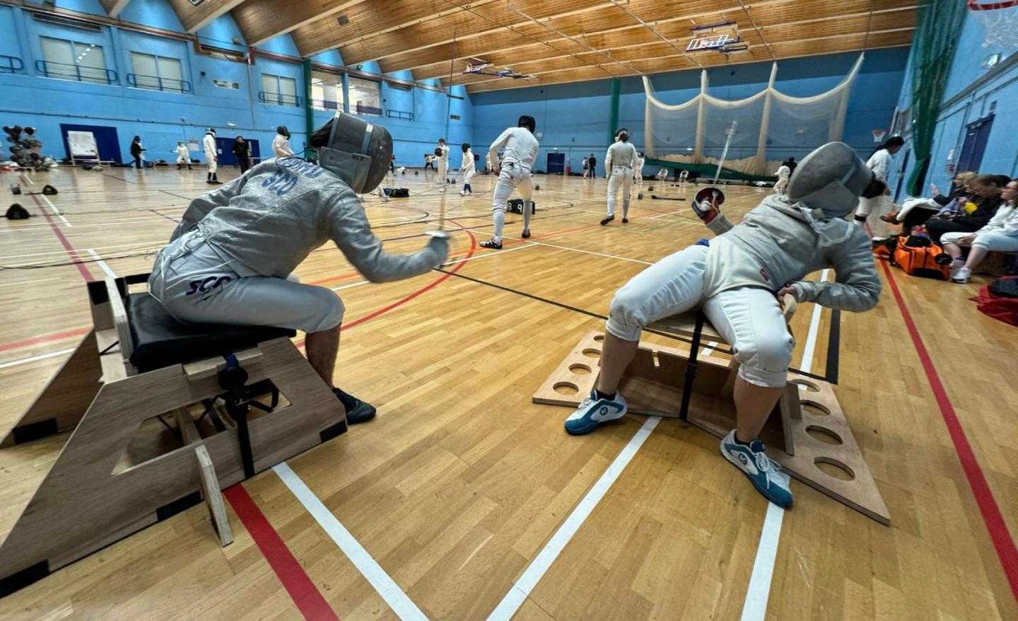 2 seated fencers, in full attire and mid bout, using the new SwordSeat.