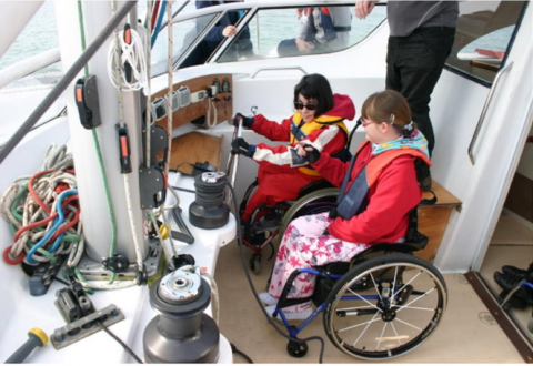 two young female sailors in wheelchairs steering the yacht