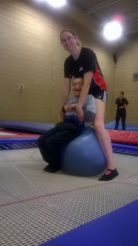 Coach helping participate to bounce on the trampoline using a gym ball