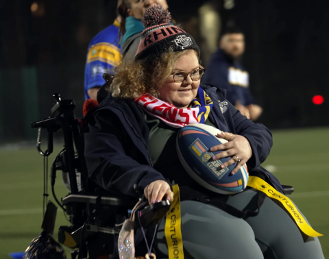 Female electric wheelchair user in hat and scarf, playing a game of touch rugby league