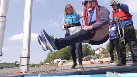 Dock side hoist being used to help lower a participant into a sailing boat.