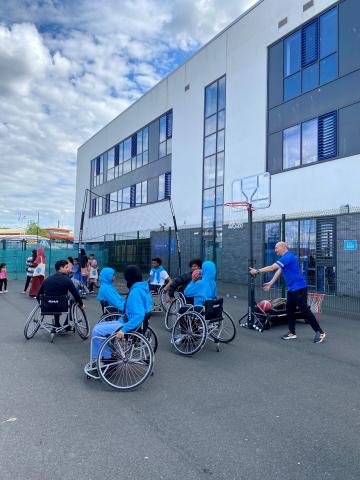 Group of disabled and non-disabled school children playing wheelchair basketball together on a school playground.