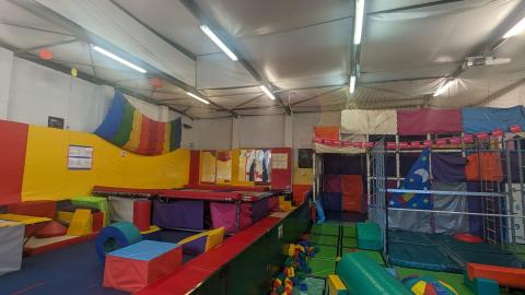 The main gym at Jump Space. The floor is lined with colourful mats. On the left are two trampolines, and on the right is a soft play gym.
