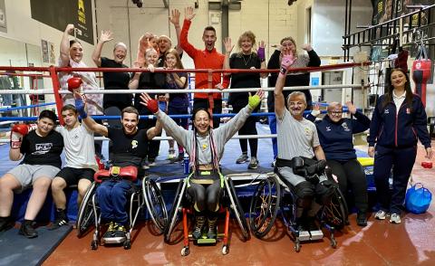 All members of Kronik Warrior adaptive boxing club, stood and sat at the ring side with arms in the air celebrating their Club of the Month award hand over.