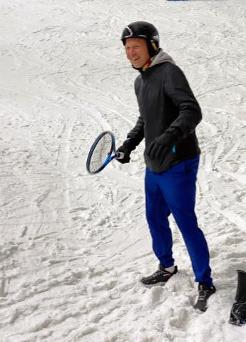 Tennis coach Ben Howarth standing on an indoor snow slope, with racquet in hand.