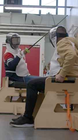 Two seated fencers engaged in a bout
