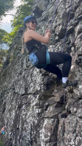 Sam, a visually impaired climber, mid ascent on a roped outdoor climbing face.