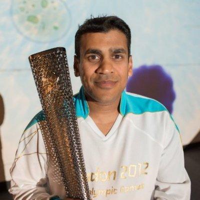 Kush a man with short dark hair, is pictured whilst bearing the Paralympic torch from London 2012 in the ceremonial white outfit.