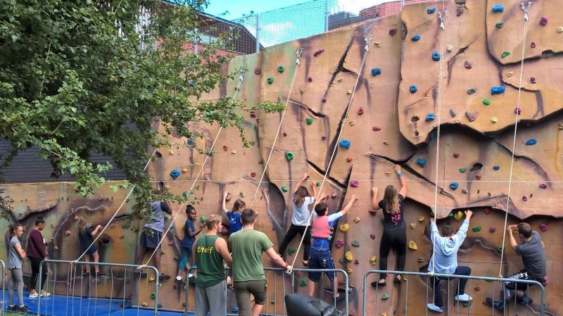 We have a small, 5meter high, 10meter wide, outdoor rock climbing wall on site. Here, a group of young people are climbing up the wall and learning how to hold the rope for each other.