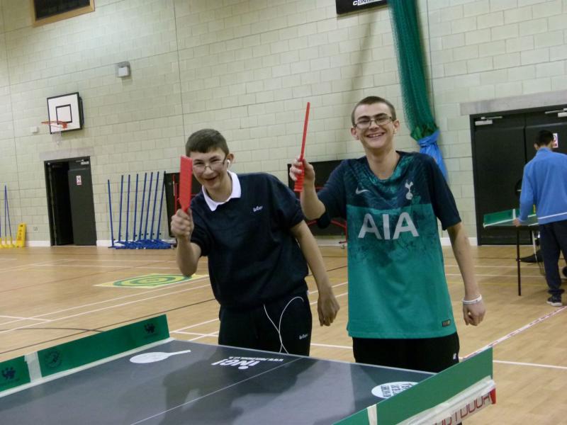 Two young table tennis players waving to camera