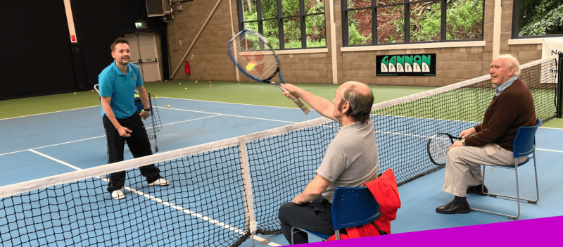 two participants sitting on one side of the net ready to receive a serve from tennis coach