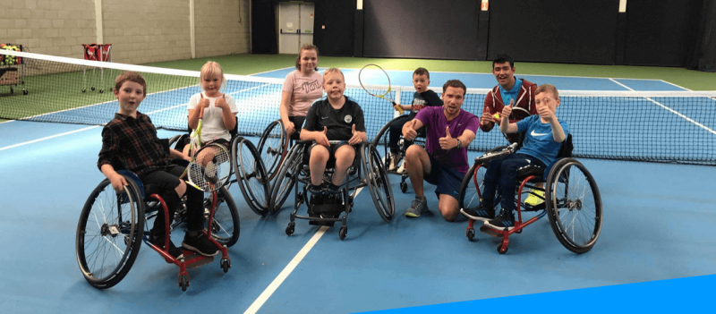 group of young children in wheelchairs with tennis rackets on the tennis court