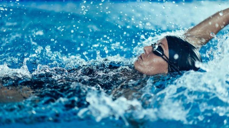 woman swimming backstroke in indoor pool