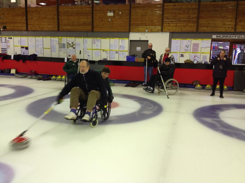 a few members in wheelchairs playing curling on ice, just pushing out the stone