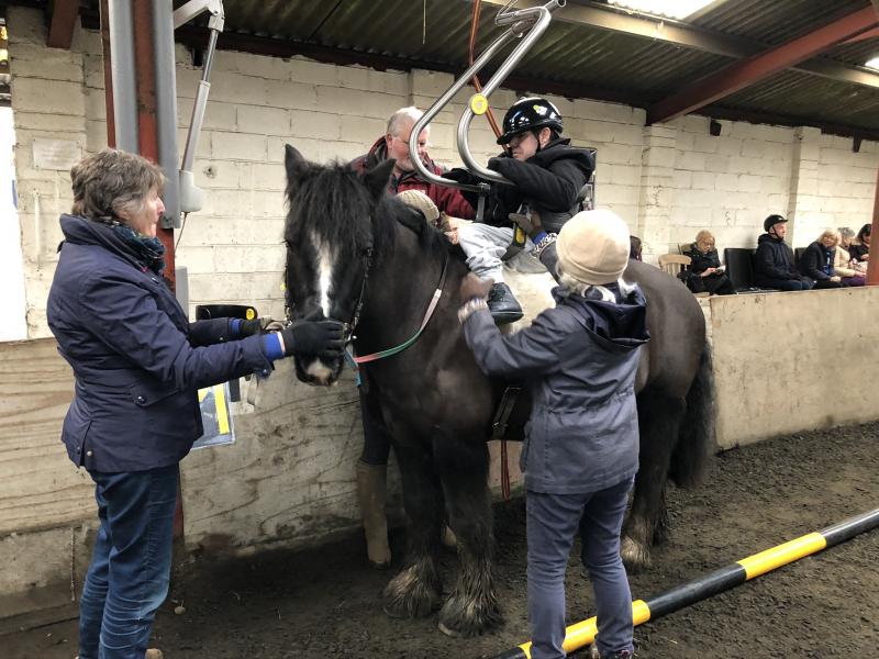 A rider with Cerebral Palsy being hoisted onto one of the ponies, being helped by three volunteers