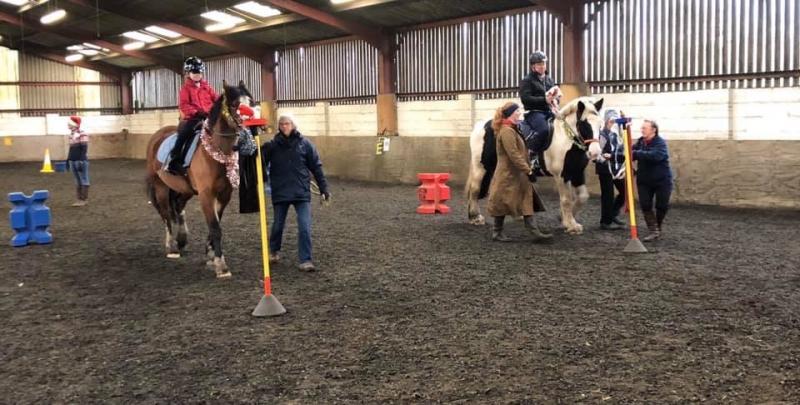 Two horses and riders in a session with volunteers helping to lead the horses around obstacles