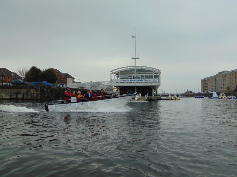 The Wheelyboat speeding through the Liverpool Docks with Liverpool Watersports Centre in the background 