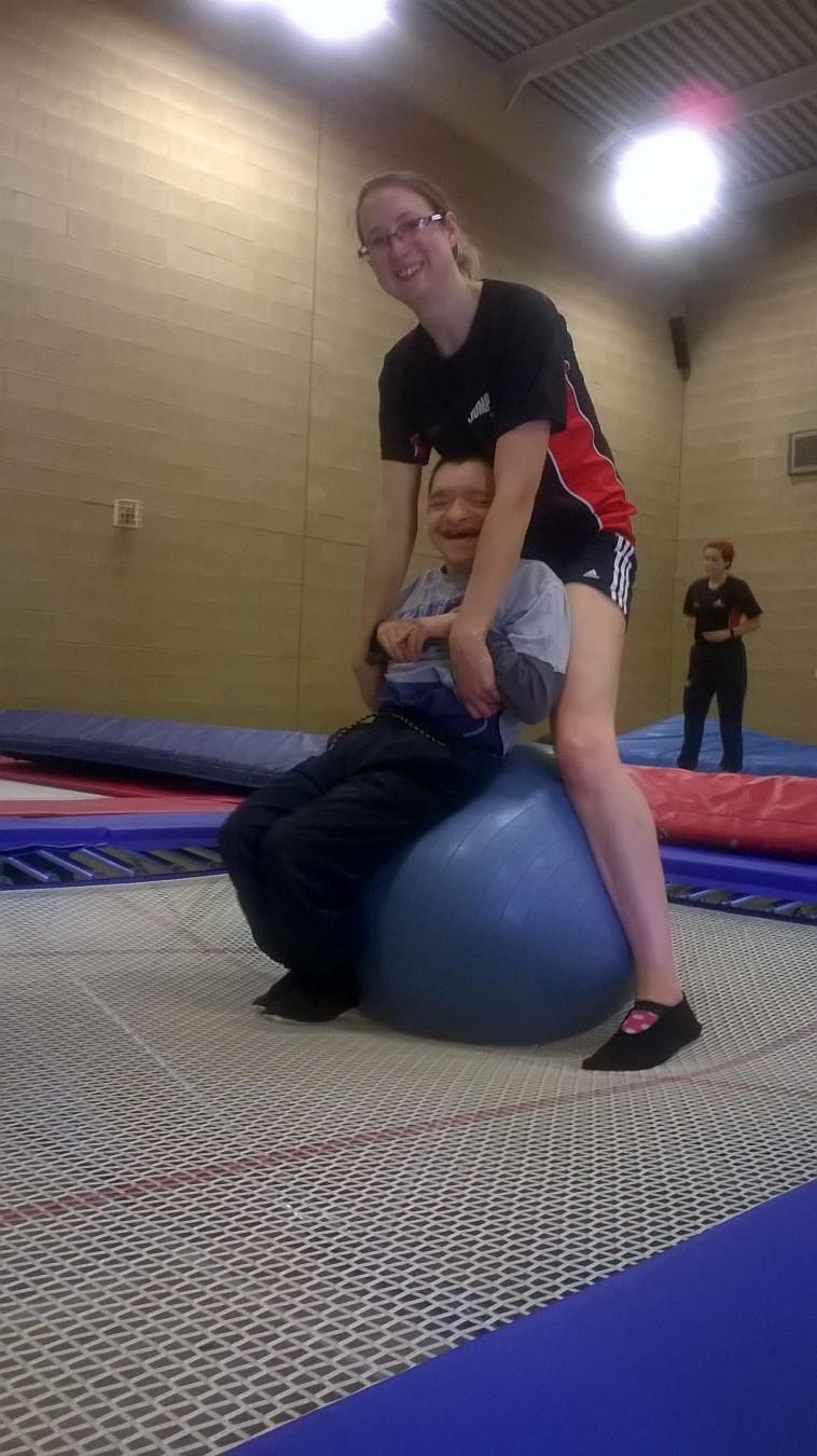 Coach helping participate to bounce on the trampoline using a gym ball