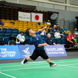 Male athlete of short stature making a winning shot over the net, leaping into the air