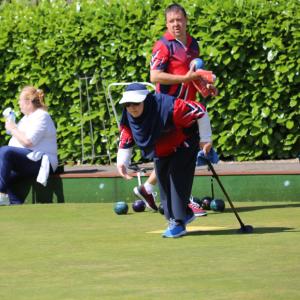 A lady leaning down about to throw her bowl onto the green