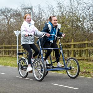 Two girls on a tandem bike, biking down a road with smiles on their faces