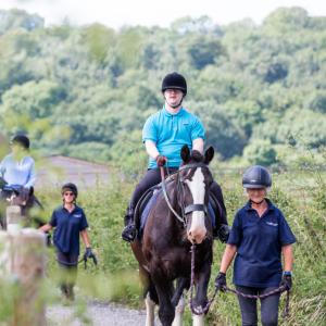 Two disabled riders being led on horses along a country lane