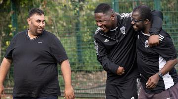 Group of 3 adaptive footballers walking together, hugging smiling and lauging.