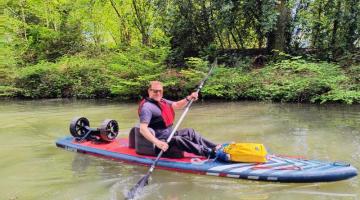 A man on an adapted seat paddleboard on a river on a sunny day