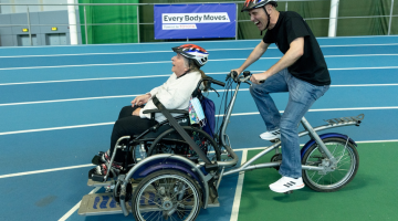 A man biking pushing a lady in a wheelchair around the track