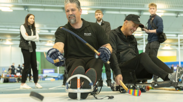 A man in an adapted seat playing curling with a group of people behind