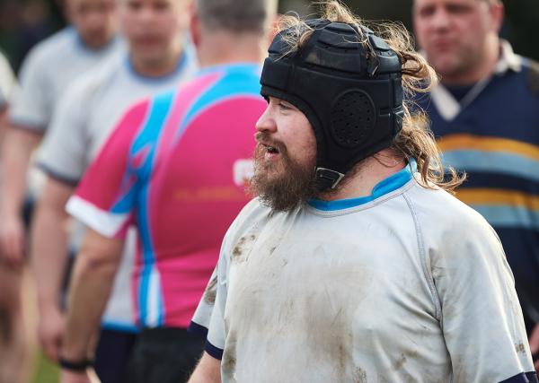 A male rugby player with a beard wearing a scrum hat in the midst of a game.