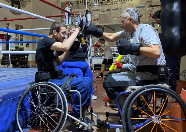 Kronik Warrior adaptive boxing club of the month cover image. Showing two wheelchair users, wearing boxing gloves and sparring at the side of the ring