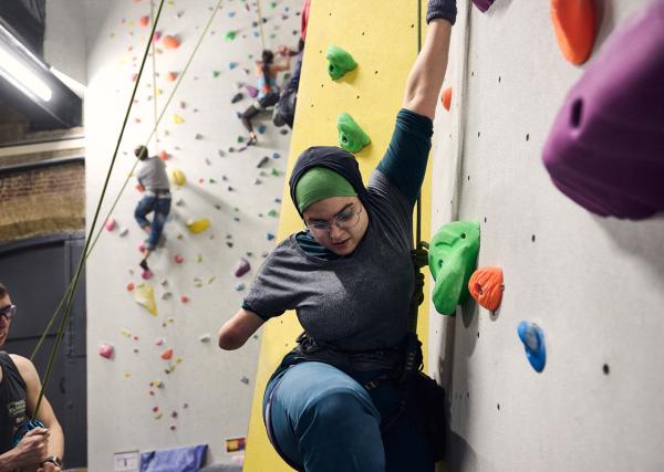 An adaptive climber mid climb on an indoor wall.
