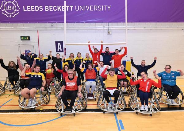 Group of participants at the Club of the Year handover event, stood and sat in wheelchairs in front of a set of training size rugby posts. Hands in the air celebrating.