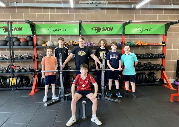 A group from Strength Academy Wales stood and sat around a bench press rack.
