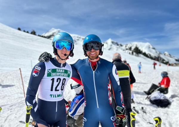 Sam Cozens and guide Adam Hall on a snow-covered mountain slope. Adam has his arm around Sam and they are both looking at the camera.