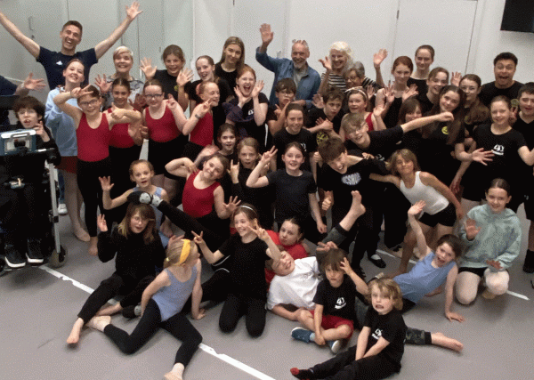 Full group shot of Cairngorm School of Dance participants in a mixture of stood and sat poses, all smiling and waving towards the camera.